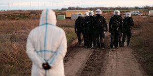 eine Person in weißem Ganzkörperanzug steht einer Gruppe Polizisten gegenüber