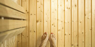 Aufnahme von oben: nackte Füße mit rot lackierten Zehnägeln über Holzboden. Auch die Wände sind auf Holz