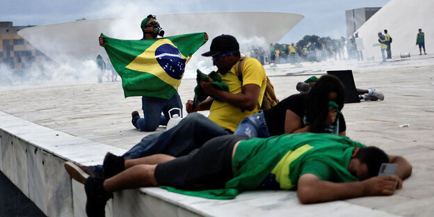 Vier Personen mit brasilianischen Nationalflaggen knien, sitzen und liegen am Rand eines Dachs