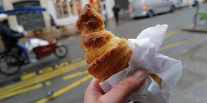 Eine Hand hält ein Croissant auf einer Straße in Paris