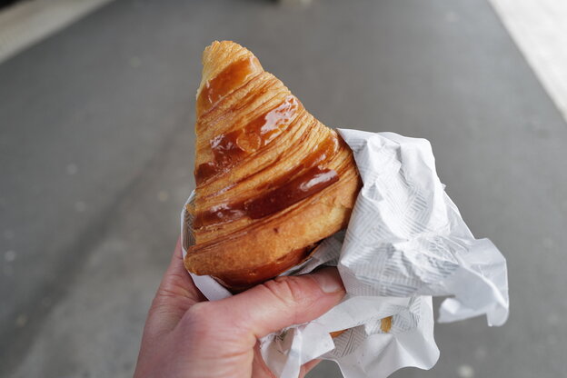Eine Hand hält noch ein Croissant auf einer Straße in Paris Eine Hand hält noch ein Croissant auf einer Straße in Paris