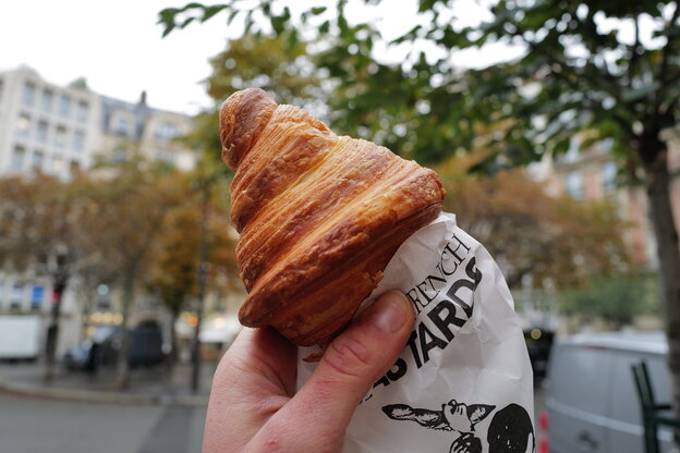Eine Hand hält ein weiteres Croissant auf einer Straße in Paris Eine Hand hält ein weiteres Croissant auf einer Straße in Paris