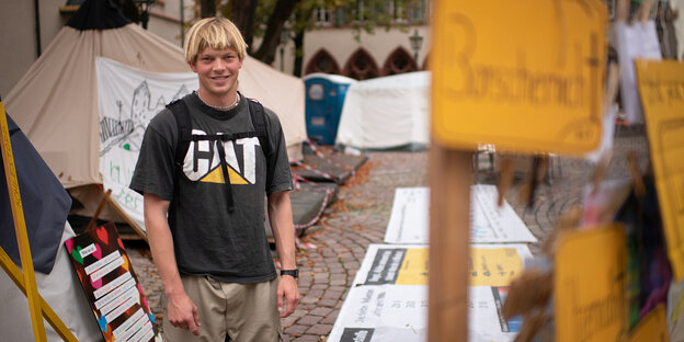 Portrait of Lucas Zander between tents and posters in front of the climate camp in Freiburg