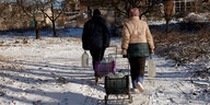 2 Personen gehen mit Einkaufswagen beladen mit Wasserflaschen durch den Schnee