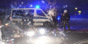 Das Bild zeigt ein Polizeiauto und mehrere Polizisten hinter explodierenden Feuerwerkskörpern.