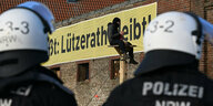 Ein Demonstrant sitzt bei der Räumung des Dorfes Lützerath auf einer Holzkonstruktion vor einem Plakat mit dem Slogan "Lützerath bleibt!".
