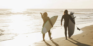 Zwei Menschen am Strand halten ihr Surfbrett unterm Arm