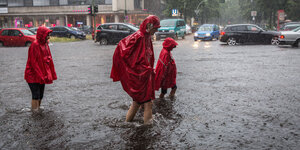Menschen in Regencapes überqueren bei Regen eine überflutete Straße in Berlin