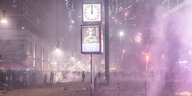 Eine Uhr auf einer Straße zeigt Mitternacht, im Hintergrund Feuerwerk