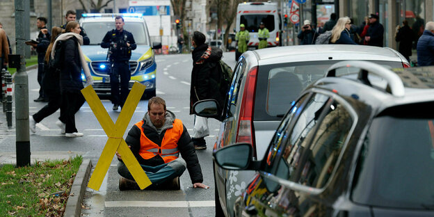 An activist wearing a safety vest blocks a road and holds a yellow wooden cross in his hand
