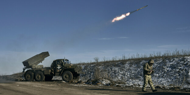 A soldier stands in front of a firing rocket launcher