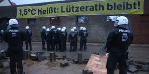 Polizisten in Uniform und mit Helm stehen vor einem Plakat, auf dem steht: 