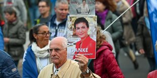 Ein mann ist zwischen anderen Demonstrierenden zu sehen, er hält ein Foto von Sahra Wagenknecht in der Hand