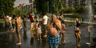 Menschen auf der Straße, die sich in Badekleidung von Wasserfontänen nassspritzen lassen
