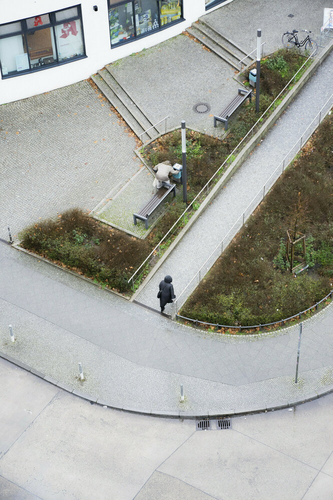 Blick auf eien Vorplatz von oben, jemand wühlt im Müll neben einer Bank