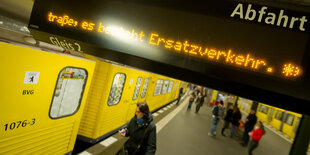 Person schaut vor Berliner U-Bahn aufs Smartphone. Auf der Anzeige drüber steht "Ersatzverkehr"