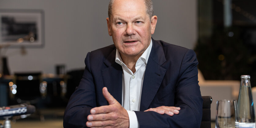 Olaf Scholz spricht. Er sitzt an seinem Schreibtisch im Kanzleramt