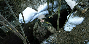 Ein Soldat steht mit Helm in einem Schützengraben und raucht eine Zigarette