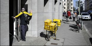 Ein Postbote steht vor einer Haustür in Berlin, sein Fahrrad ist auf dem Gehsteigabgestellt