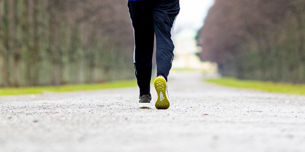 Ein Jogger läuft bei trübem Wetter durch eine Allee.