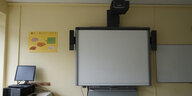 In einem Klassenzimmer hängt ein Whiteboard mit Beamer an der Wand. Daneben steht ein Computer.