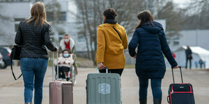 Drei aus der Ukraine stammende Frauen von hinten zu sehen, laufen mit Rollkoffern eine Straße hinunter