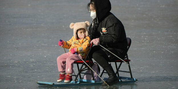 Eine chinesische Frau mit Kind fährt auf einem zugefrorenen Teich.
