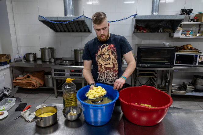 Ein junger Mann steht in einer Großküche und bereitet Essen ,vor ihm geschnittene Kartoffeln