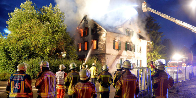 Feuerwehrleute vor einem brennenden Haus.