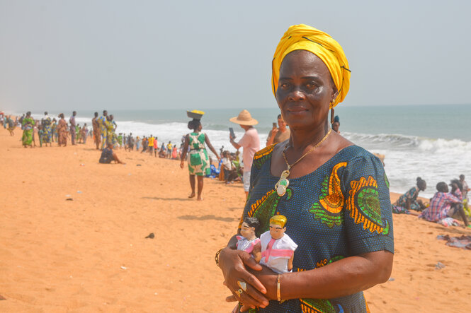 Eine Frau steht am Strand, in der Hand hält sie Puppen