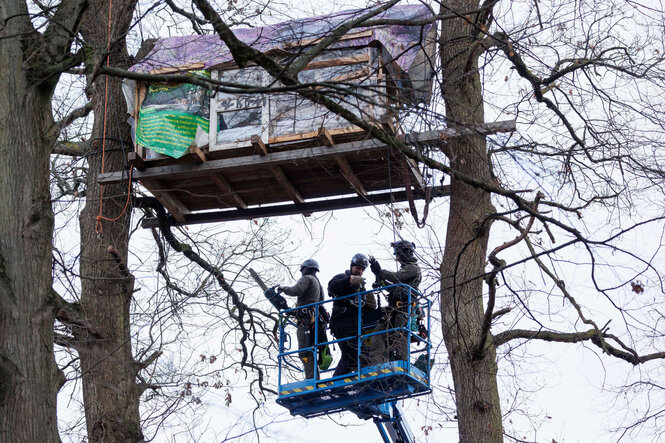 Drei Polizisten nähern sich auf einer Hebebühne einem Baumhaus