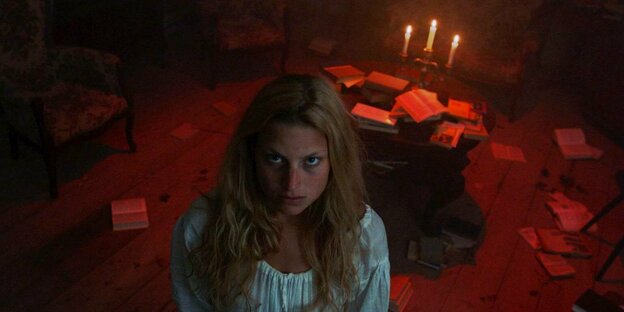 Eva (Anna Platen) steht im weißen Kleid in einem von Kerzen beleuchteten Raum.