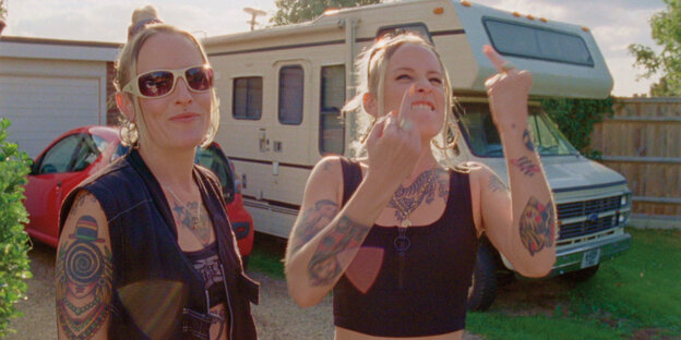 Twin sisters Polly and Sophie Duniam are standing in front of their mobile home, one with her middle fingers raised.