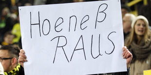 Das Foto zeigt ein Plakat, auf dem "Hoeneß raus" steht, hochgehalten von einem Fußballfan.