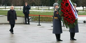 Putin geht auf einen großen kranz mit Rosen zu, der von 2 Soldaten gehalten wird
