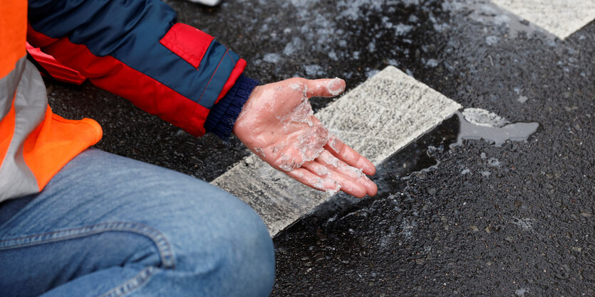 Eine Person hat sich mit der Hand auf eine Straße geklebt.