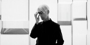 Ryuichi Sakamoto vor einigen Spiegeln oder verspiegelten Fenstern