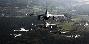 Kampfflugzeuge fliegen in einer Formation über eine Landschaft