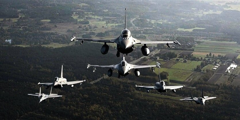 Kampfflugzeuge fliegen in einer Formation über eine Landschaft