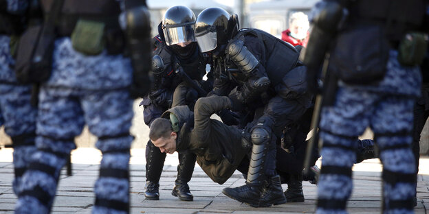 Einem jungen Mann werden bei seiner Verhaftung die Arme verdreht. Die Polizisten tragen martialische Tarnanzüge und Helme