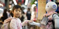 Ein Kind reicht einem Roboter die Hand