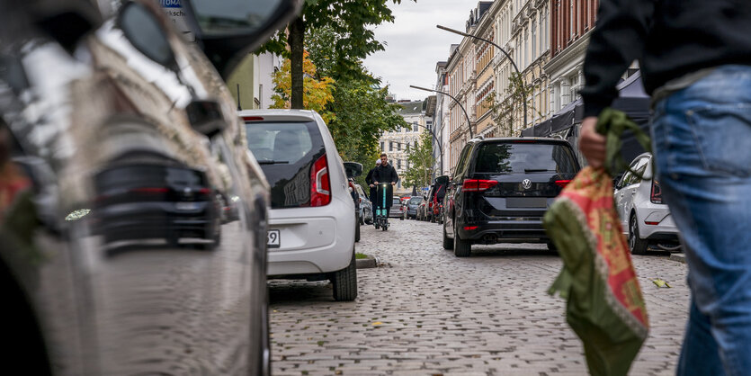 Zwei Rollerfahrer fahren zwischen zwei Reihen dicht geparkter Autos entlang