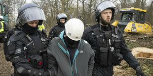 Mehrere Polizisten und in der MItte eine mit weißem Helm vermummte Person