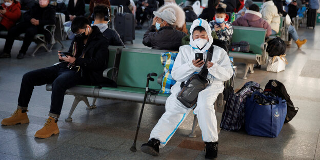 Many people in a waiting room, one of them in a protective suit