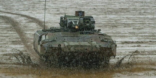 A Puma armored personnel carrier drives across the muddy training ground during a combat demonstration