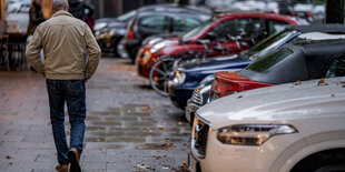 Ein Mann geht auf dem Gehweg, neben ihm parken Autos mit den Vorderrädern auf dem Gehweg