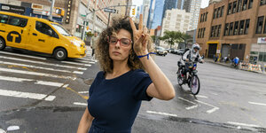 Masih Alinejad steht auf einer Straßenkruezung in New York und macht das Victory Zeichen