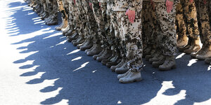 Zwei Reihen von Bundeswehrsoldat*innen stehen dicht beieinander. Man sieht nur ihre Beine und Stiefel. Sie werfen Schatten.