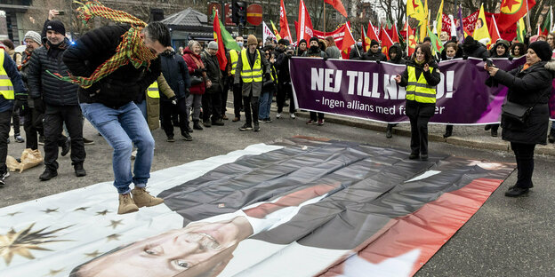 Ein Mann springt auf einem großen Erdogan-Plakat auf dem Boden während im Hintergrund eine Demo mit Fahnen ist
