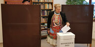 Eine Frau in Tracht wirft einen Stimmzettel in eine Box mit der Aufschrift Referendum 2023